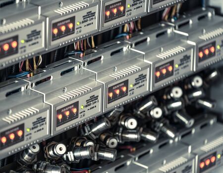 Numerous round metal plugs connected to each other by wires hang between panels illuminated by...