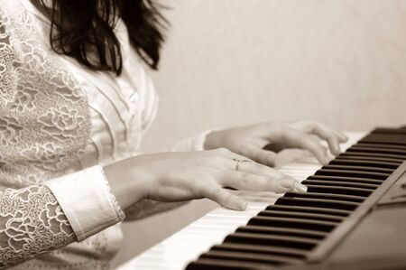 Female hands on piano. Brunette woman in white blouse playing musical composition. Gold ring on fingerの写真素材