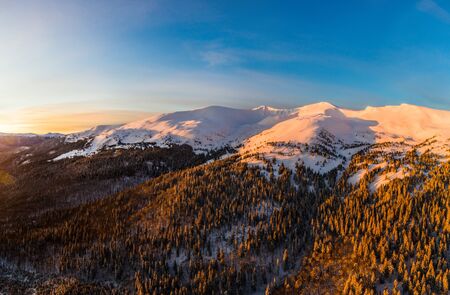 Top view of a magical view of a mountain winter forest with thick fir trees and hills in a beautiful pink winter sunset. Nordic Beauty Concept. Copyspaceの写真素材