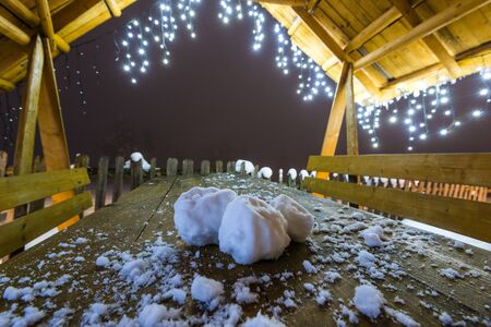 Close-up three snowballs lie on a wooden table under roof of arbor with New Year's lights....
