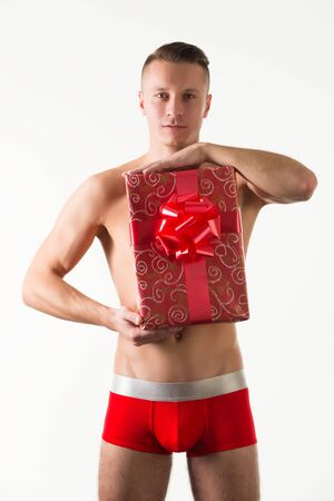 Young caucasian man model in red mens underpants standing and holding present boxes in hands over light background in photo studio. Bright mens underwear conceptの写真素材