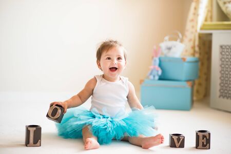 Beautiful little girl in a blue puffy skirt sits on the floor in a cozy living room with LOVE cubes. Healthy and happy children concept. Advertising spaceの写真素材
