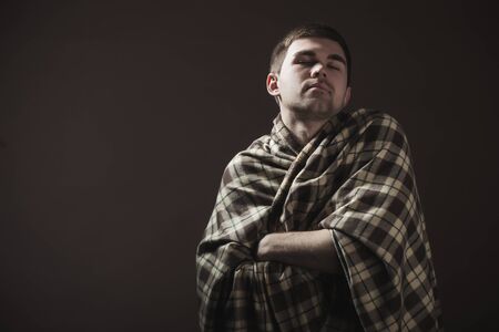 Portrait of a young sleepy man wrapped in a plaid. Concept of a hard morning awakening and working moodの写真素材