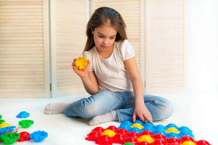 Little curious girl lays plastic puzzles on the floor sitting in her children's room. Early childhood development conceptの写真素材