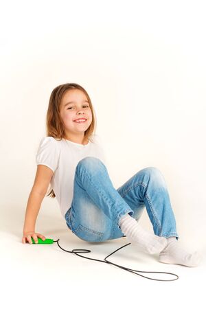 Little cheerful girl in casual clothes plays with a skipping rope and laughs while looking at the camera on a white background in the studio. Children activity concept. Advertising spaceの写真素材