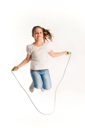 Cheerful girl in casual clothes jumping on rope and laughing while looking at the camera on a white background in the studio. Children activity concept. Advertising spaceの写真素材