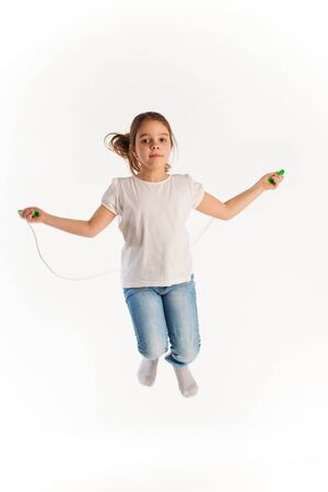 Cheerful girl in casual clothes jumping on rope and laughing while looking at the camera on a white background in the studio. Children activity concept. Advertising spaceの写真素材