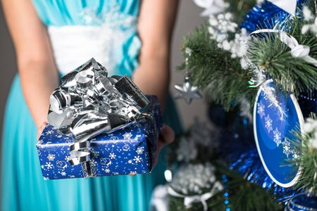 An unidentified little girl with a gift box in her hand stands next to a Christmas tree. Concept come true dreams and sale in a children's storeの写真素材