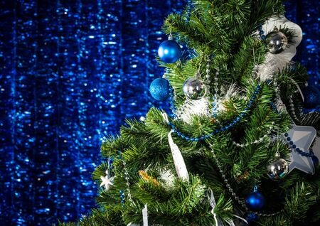 Two beautiful Christmas trees, white and green with blue Christmas toys, stand against the backdrop of blue tinsel. The concept of celebrations and traditional holidays. Advertising spaceの写真素材