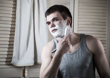 Portrait of a young man shaving his face in the bathroom during morning hygiene. The concept of a...