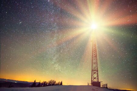 Mesmerizing landscape of the starry night sky with a radiant satellite tower spread over a snow-covered hill at the top of the mountain. Concept of weather station and beauty of the northern natureの写真素材