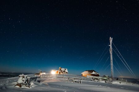 Meteorological or tourist station with a satellite tower and a harsh winter country located on a hilltop in a frosty winter night against a starry sky. Place for advertisingの写真素材