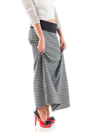 Unidentified young woman in a short white sweater and a long skirt and high heels posing on a white background. Concept of stylish women's clothing. Advertising spaceの写真素材