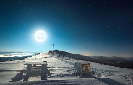 Beautiful view of the big moon and the starry sky over the snowy hilly forest terrain. Concept ski resort at night. advertising spaceの写真素材
