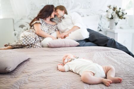 Sleeping little newborn baby lies on the bed against a background of loving blurry young parents in...
