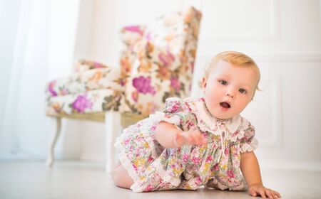 Charming little girl in floral dress crawls on floor of a beautiful stylish living room. the concept of world cognition and and the curiosity of young children. oncept of children's promotional itemsの写真素材