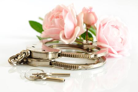Close-up chrome handcuffs and keys lie on a white table next to two pink flowers. Concept of voluntary slavery concept BDSM games. Advertising spaceの写真素材