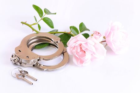 Close-up of metal handcuffs, keys and romantic pink flower isolated over white background. Sexual games and practicing bdsm conceptの写真素材