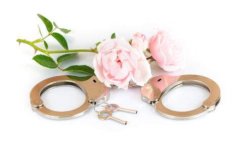 Close-up chrome handcuffs and keys lie on a white table next to two pink flowers. Concept of voluntary slavery concept BDSM games. Advertising spaceの写真素材