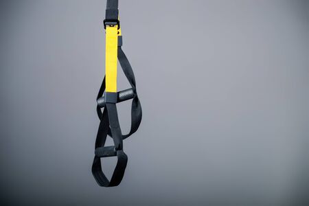 Sports suspension belts are hanging in the studio on a gray background for doing sports crossfit aerobics and aero yoga. Sports Concept. Advertising spaceの写真素材