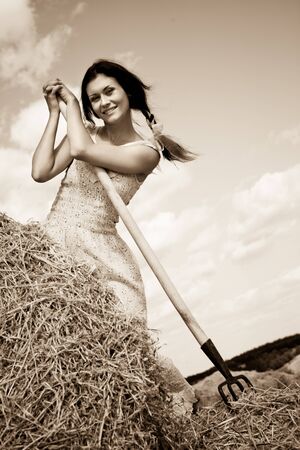 Young smiling brunette woman in dress standing with hay pitchfork in handsの写真素材