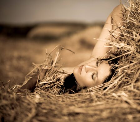 Portrait of young naked woman relaxing in dry hay
