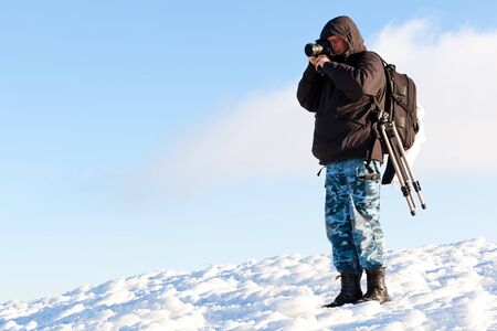 Young man photographer in winter clothing standing and making photo in sunlightの写真素材