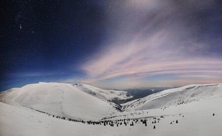 Panoramic night view of winter mountain valley covered with snow, mountains and moon in above on...