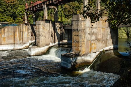 Dam standing on the river restrains a stormy river flow against the backdrop of green trees on a sunny, warm day. Concept flood protectionの写真素材