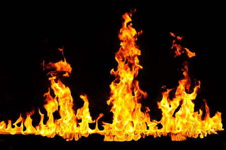 Fiery yellow orange tongues on dark background rise up, burning flame, fire close-up photo