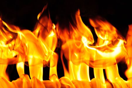 Close-up photo of bright orange yellow flame on a black background, fire burns backdrop