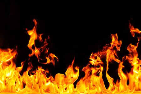 Fiery yellow orange tongues on dark background rise up, burning flame, fire close-up photo