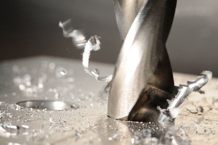 Close-up photo of drilling process with tools and metal shavings. Blurred gray background
