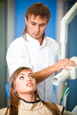 Young woman patient sitting in dentist chair and waiting for procedure with dentist doctor man in uniform at backgroundの写真素材