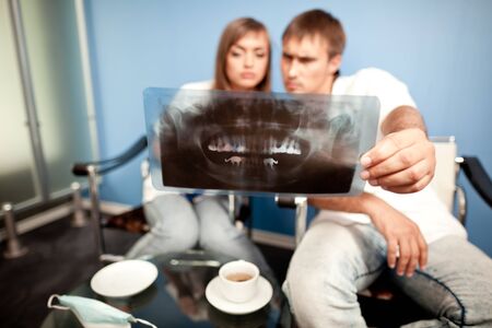 Young couple man and woman sitting in dental clinic, looking at dental picture and drinking teaの写真素材