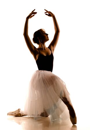 Silhouette of young beautiful ballerina in white tutu and pointe shoes doing dancing pose over white background. Ballet, grace, beauty, art conceptの写真素材