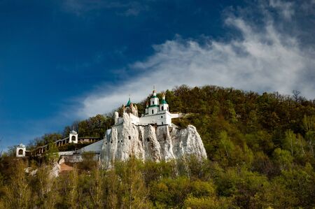Beautiful scenic view of the monastery located on a hill covered with green trees and shrubs on a warm summer day against a cloudy sky. Concept pilgrimage and spiritual cleansingの写真素材