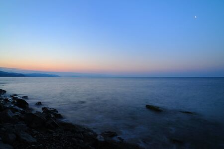 Beautiful landscape, sunset by the sea, sun rises from behind the mountains, beach is strewn with stonesの写真素材
