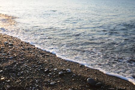 Sunset on seashore, rocky beach and blue sky. Small hills covered with green plants in backgroundの写真素材