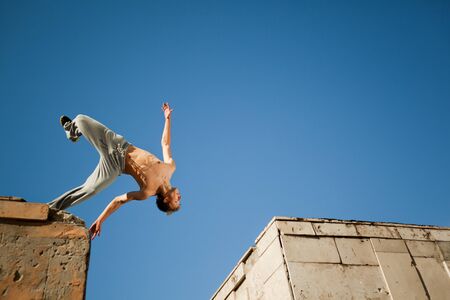 Young man jumping and practicing parkour between two buildings outside on clear summer day with blue sky at background. Active lifestyle and extreme sports conceptの写真素材