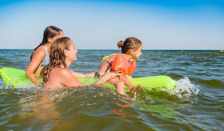 Happy mother and two small positive daughters bathe and swim in the sea with an air mattress on a sunny summer day. Vacation concept with kids. Copyspaceの写真素材