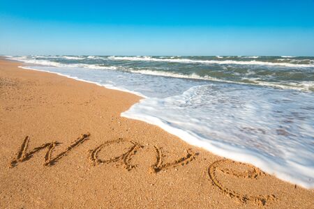 Inscription wave on the wet sand near the splashing blue sea wave on a sunny hot summer day. Tropical Country Vacation Concept. Copyspaceの写真素材