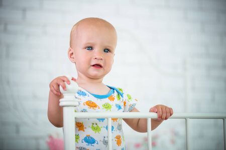 Cute little baby is standing on the edge of bed