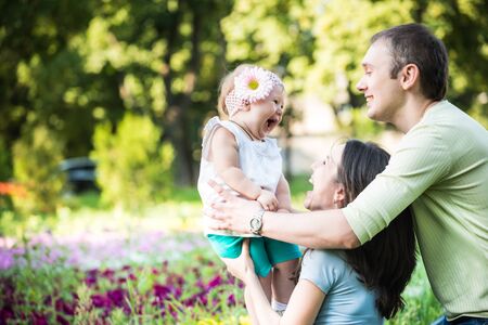 Parents walking, playing and kissing their small daughter in parkの写真素材
