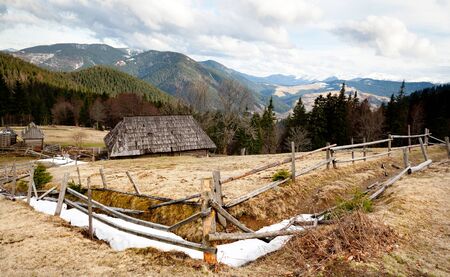 Small old wooden fence located on green hill. On background mountains and clear blue sky without cloudsの写真素材