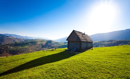 Small old wooden house among tree covered hills. Mountain landscape, coniferous forest covered with fogの写真素材
