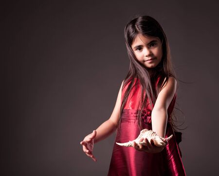 Small girl with long hair in golden red dress holding a shell in her handsの写真素材