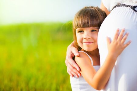 Little girl hugs mom pregnant bellyの写真素材