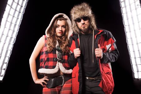Stylish couple standing against black background.