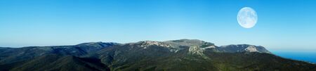 Stunning mountain landscape panorama against the blue sky and full moon in the evening. Concept of...